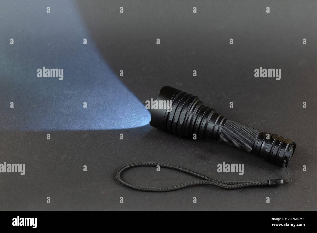 Hochleistungs-LED-Handheld-Taschenlampe beleuchtet den Raum vor Ihnen. Kleine, moderne taktische Handtaschenlampe mit einem Gurt gegen ein Grau Stockfoto