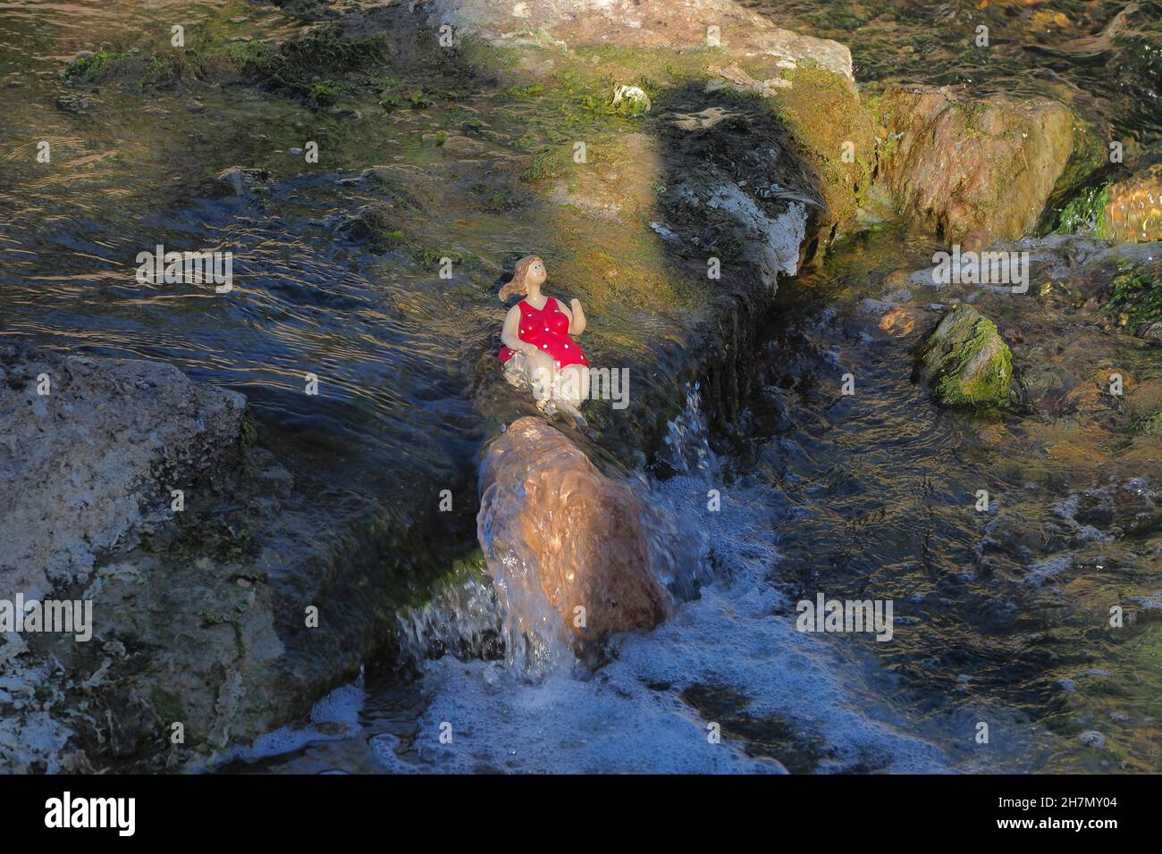 Badegäste am Wasserfall, Figur am Wasserfall, Steinfigur am Wasser, sitzende Frauenskulptur in rotem Schwimmkostüm am Wasser Stockfoto
