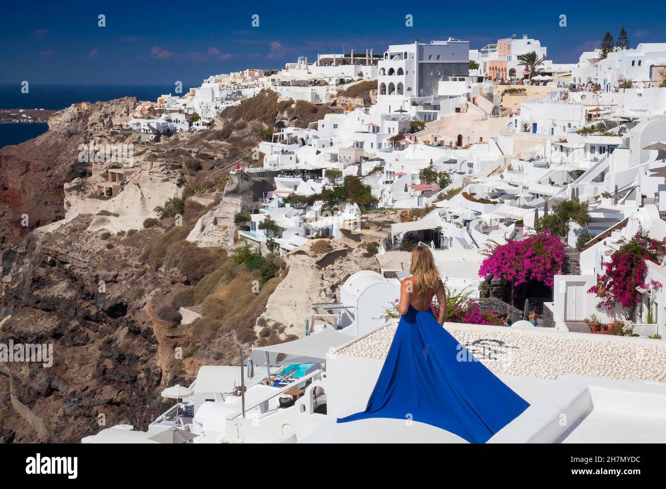 Frau in einem blauen Kleid blickt über den Ort Imerovigli, Santorini, Kykladen, Griechenland Stockfoto