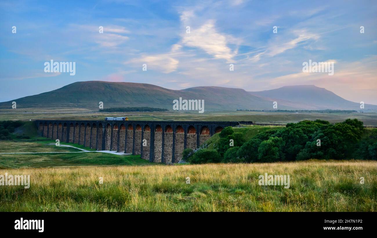 Landschaftlich reizvolle Tal- und Sonnenuntergänge (Lokomotive, Wahrzeichen Ribblehead Viaduct Torbögen, hohe Hügel und Berge) - North Yorkshire Dales, England. Stockfoto