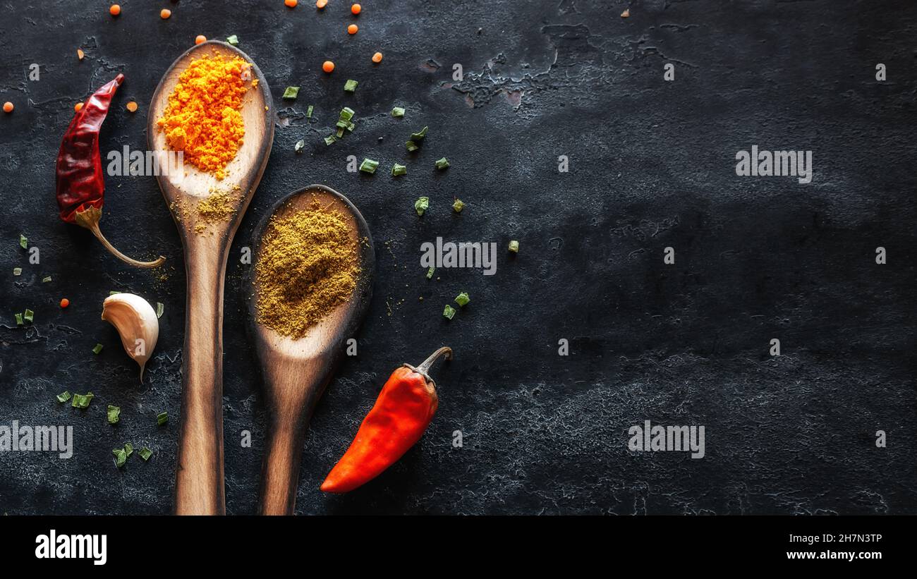 Gewürze in Holzlöffeln und trockene rote Paprika auf schwarzem Hintergrund mit Platz für Text Stockfoto