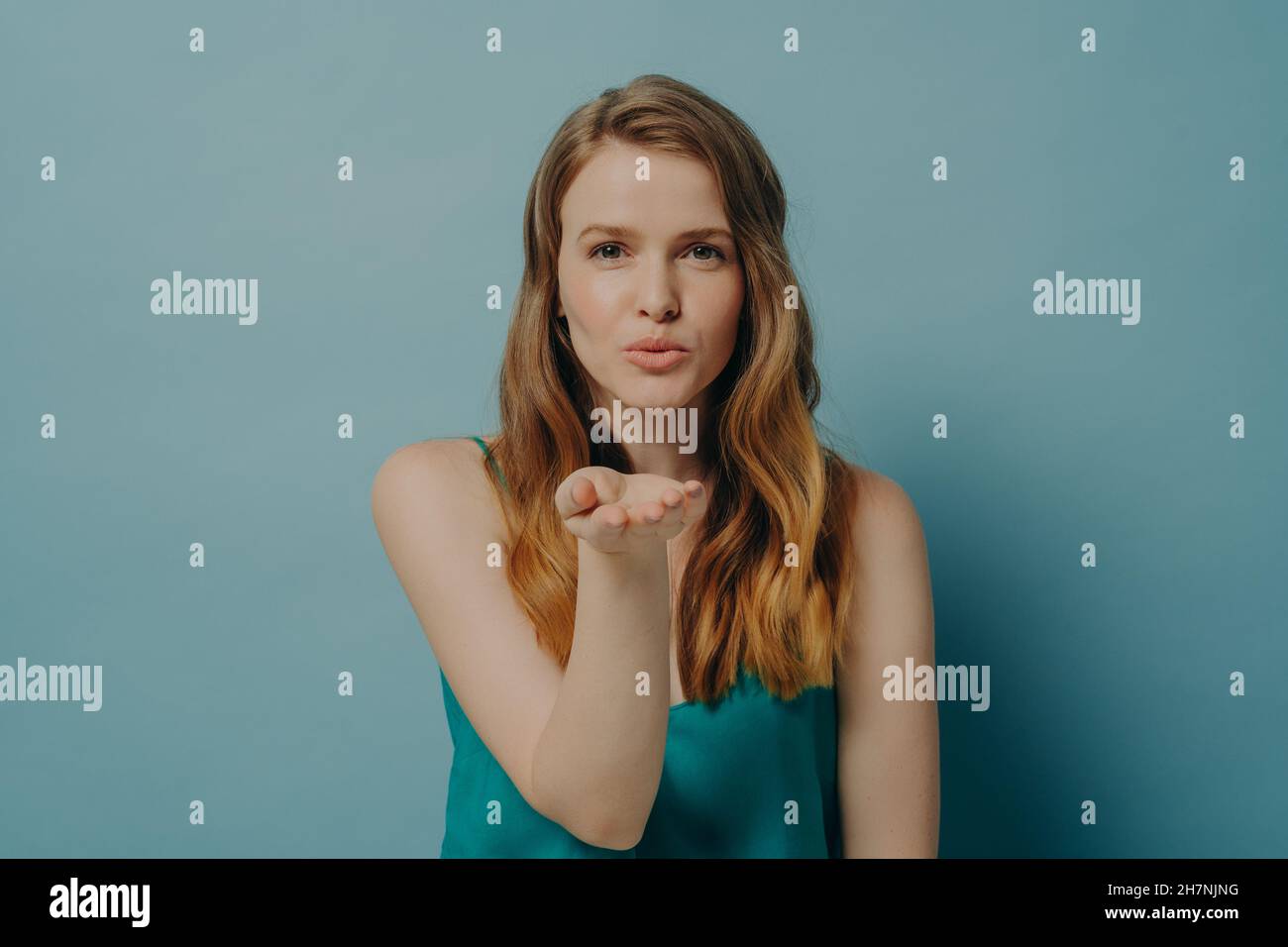 Hübsches ehrliches Mädchen, das Luftkuss bläst und Liebe zum Ausdruck bringt, während es isoliert auf blauem Hintergrund steht Stockfoto