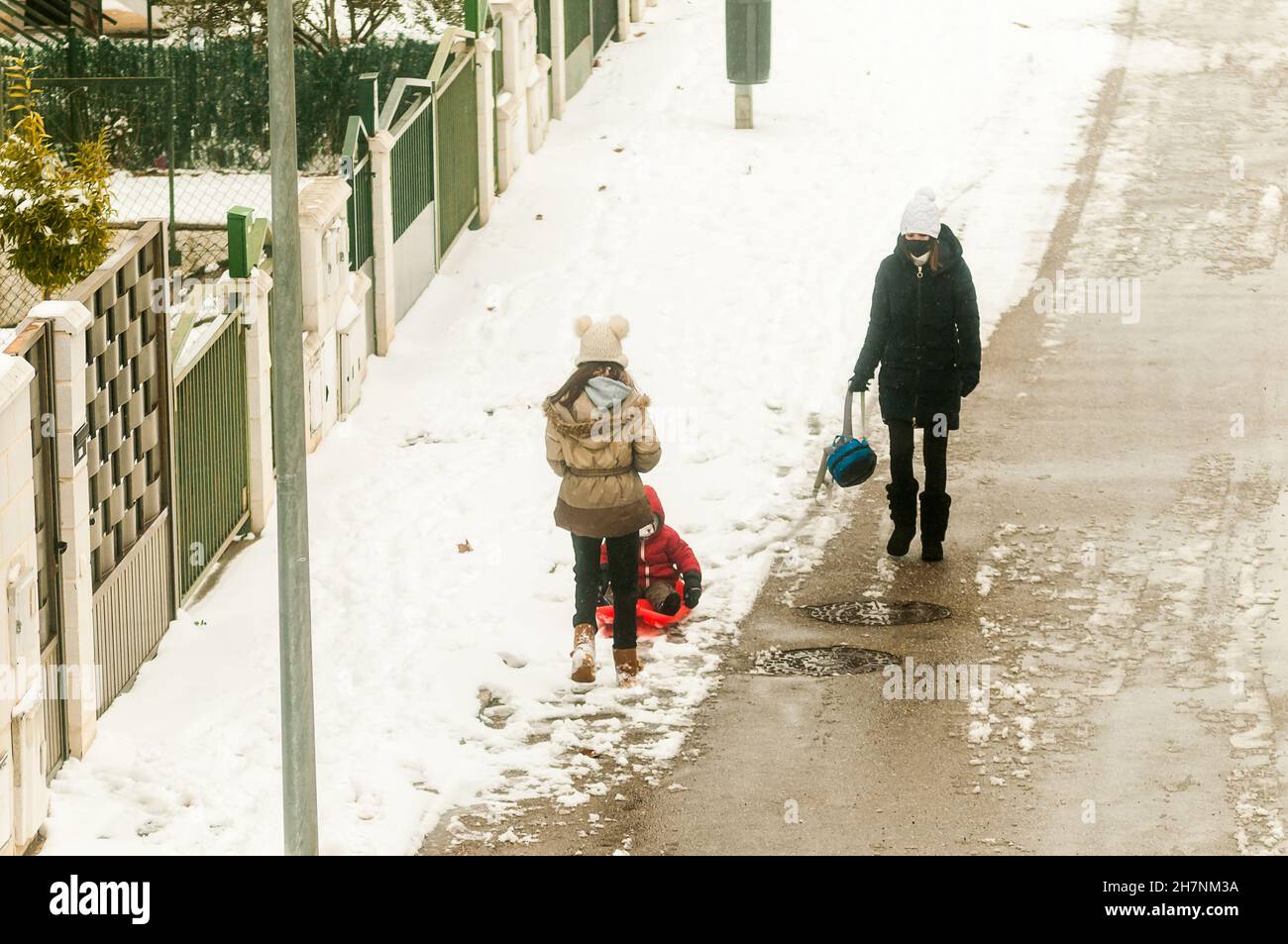 Eine warme Frau mit einem Rucksack und zwei Kindern, die während eines nebligen und verschneiten Tages im Winter in Zamora in der verschneiten Straße spielen. Stockfoto