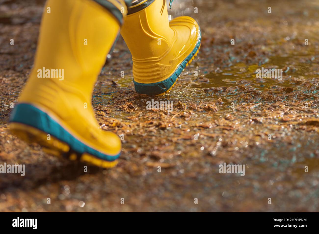 Kind mit Gummiregenstiefeln, das am Herbstnachmittag auf dem nassen Bürgersteig läuft, selektiver Fokus Stockfoto