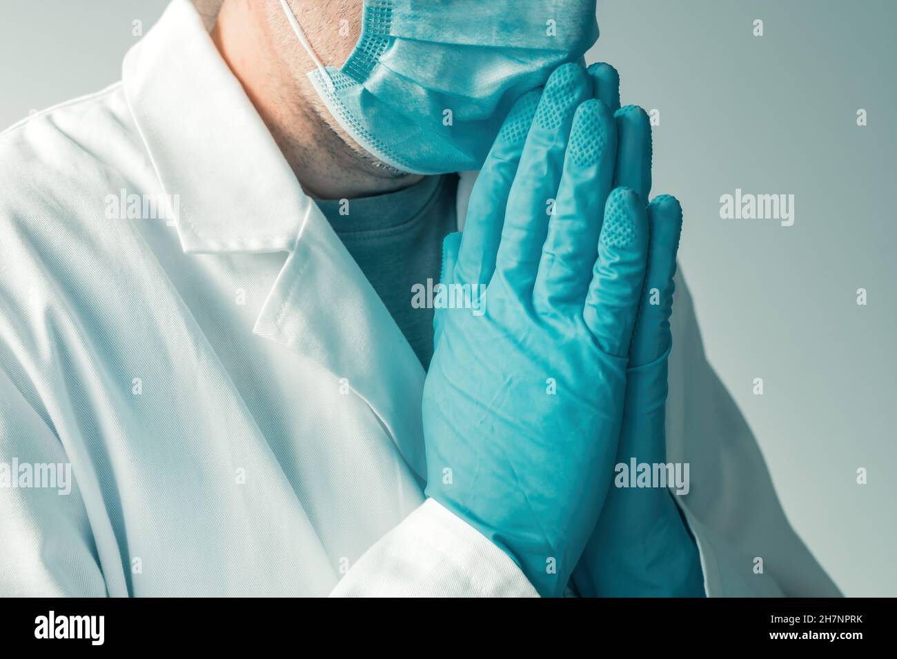 Medizinische Fachkraft trägt Schutzhandschuhe und Gesichtsmaske mit Händen in betender und flehender Position, selektiver Fokus Stockfoto