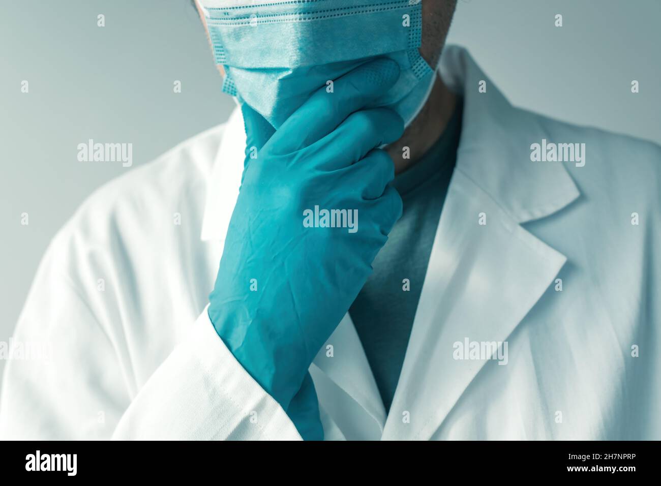 Arzt mit Schutzhandschuhen und Gesichtsmaske, die Hand am Kinn hält und denkt, selektiver Fokus Stockfoto