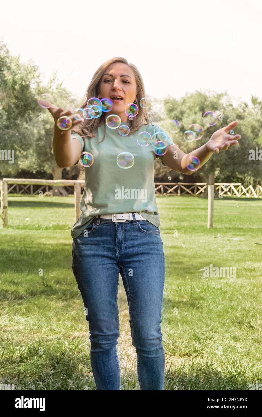 Frauen in T-Shirt und Jeans spielen mit Seifenblasen in einem Park, drei Viertel Schuss mittleren Alters kaukasischen Dame Spaß ioutdoor in einem Sommer. Ma Stockfoto