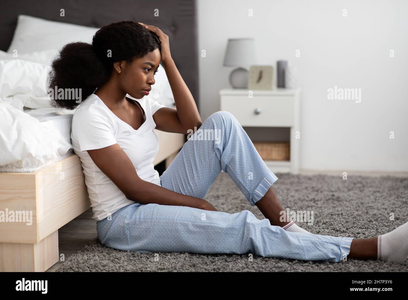 Depressive junge schwarze Frau, die zu Hause am Bett sitzt Stockfoto
