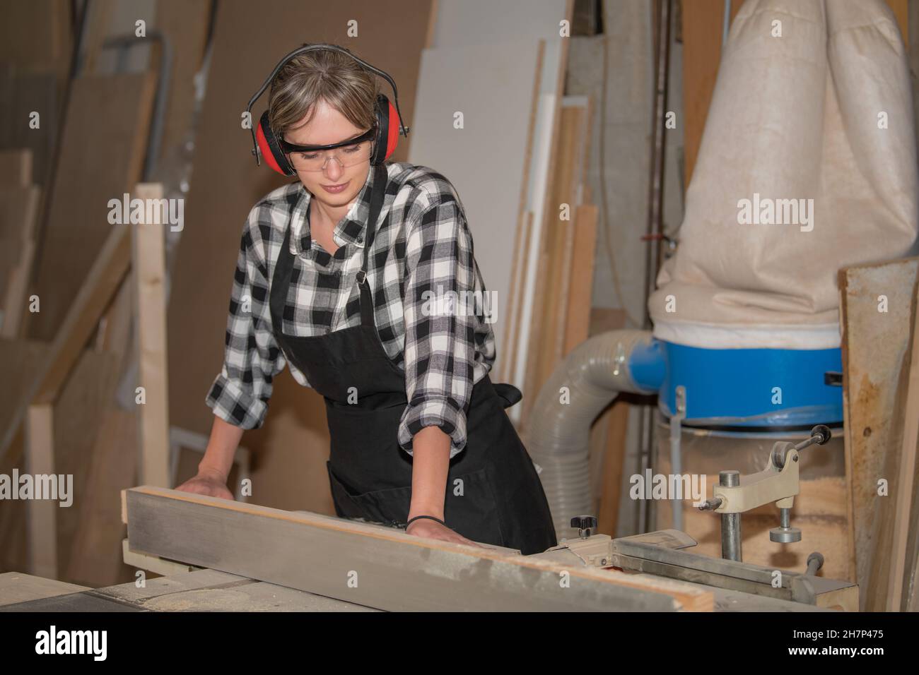 Junge Frau als Zimmermann mit Schutzbrille und Gehör Schutz funktioniert auf Hobelmaschine Stockfoto