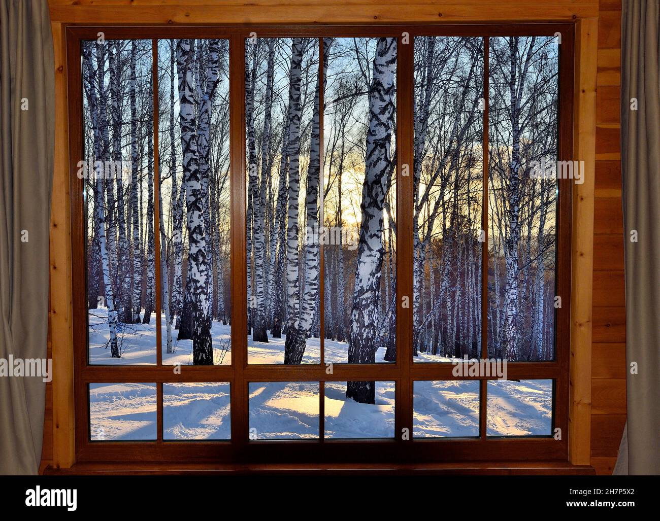 Goldener Winter Sonnenuntergang Birkenwald - Blick durch Holzfenster in warmen gemütlichen Zimmer. Winterurlaub, Weihnachts-Ruhekonzept. Winterwunderland, Märchenland Stockfoto