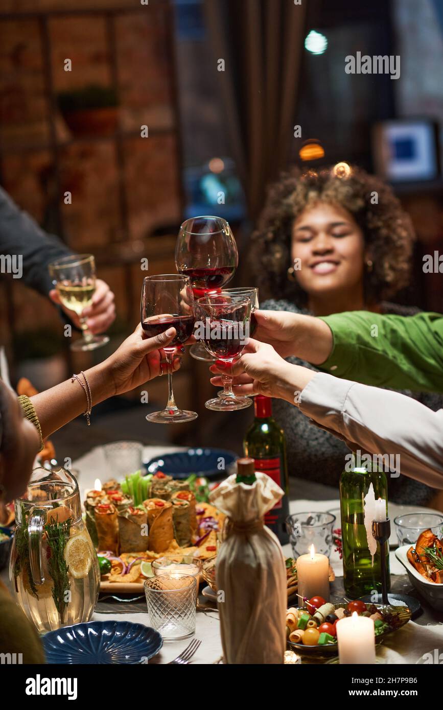 Fröhliche Leute, die mit einem Glas Rotwein rösten, während sie am Esstisch feiern Stockfoto