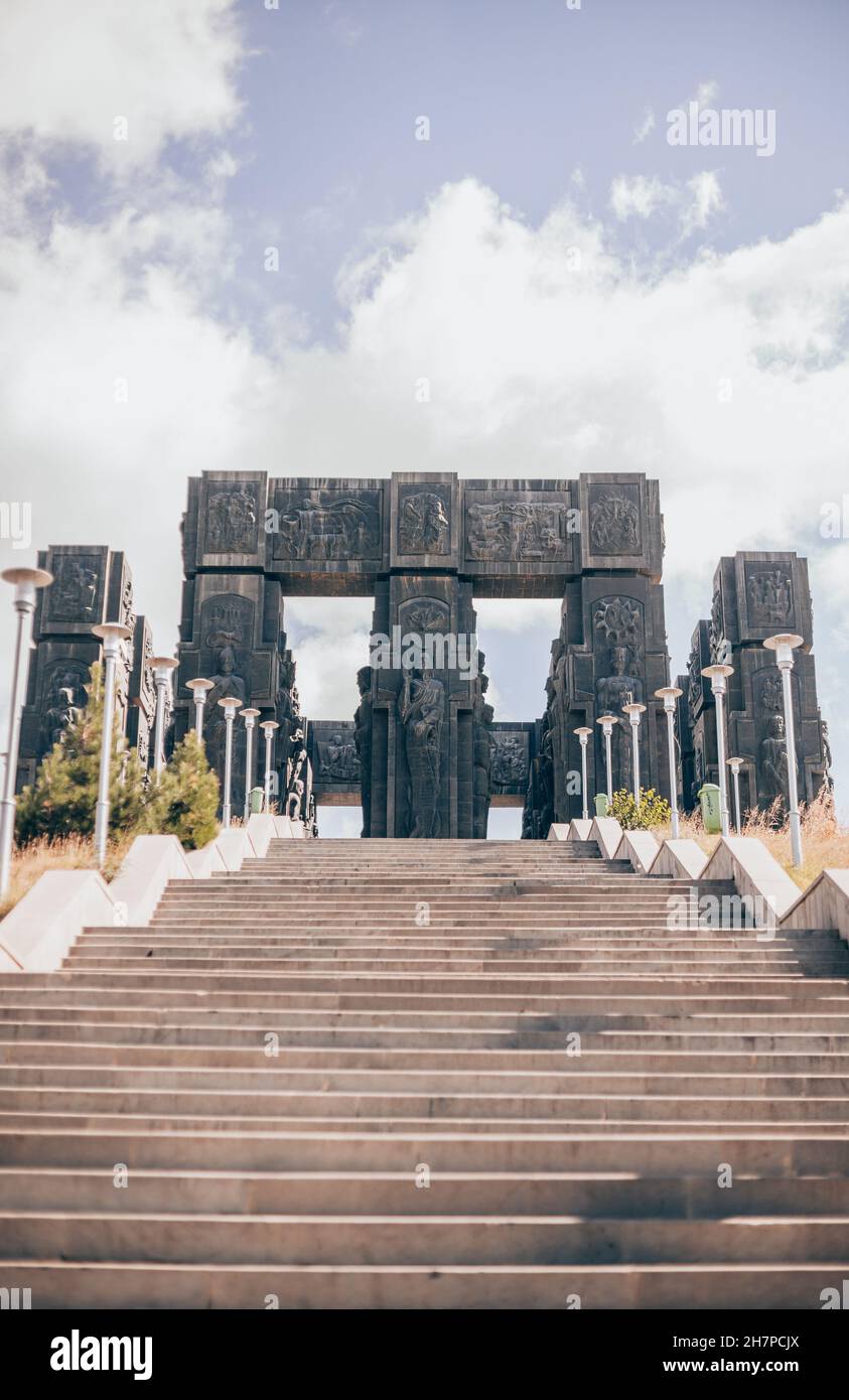 Denkmal aus dunklem Stein in Georgien. Große Treppe führt zu einem alten Bogen mit Figuren. Alte Architektur, historisches Erbe Stockfoto