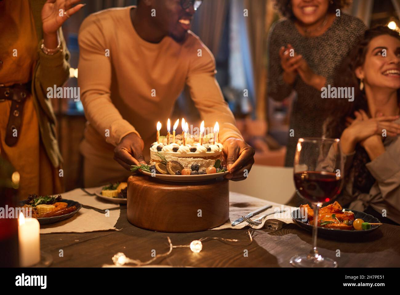 Afrikanischer junger Mann bringt Geburtstagskuchen mit Kerzen für seinen Freund während einer Geburtstagsfeier Stockfoto