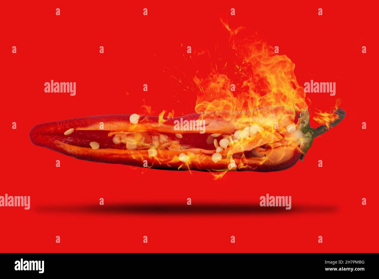 Rote, scharfe Chilischote auf Feuer, in zwei Hälften geschnitten, mit Samen aus nächster Nähe, die auf einem roten Hintergrund schweben Stockfoto