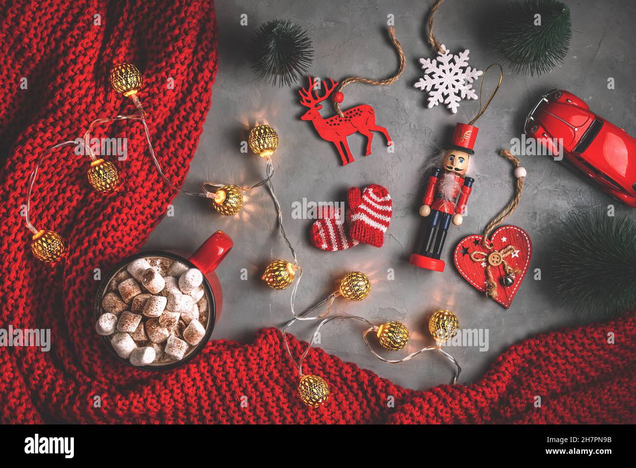 Becher mit Süssmarmelibe, Girlanden, roter Decke auf grauem Hintergrund. Neujahr, weihnachten. Spielzeug, flach liegend, Draufsicht Stockfoto