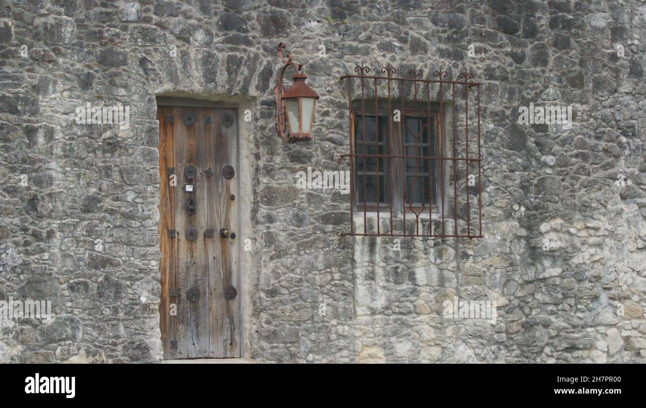 Alte graue Steinwand mit Holztür und -Fenster. Stockfoto