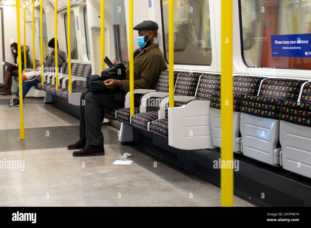 Älterer Mann, der allein in U-Bahn-TFL-Wagen sitzt, trägt eine covid Facemask mit leeren Sitzen im November 2021 London England Großbritannien KATHY DEWITT Stockfoto