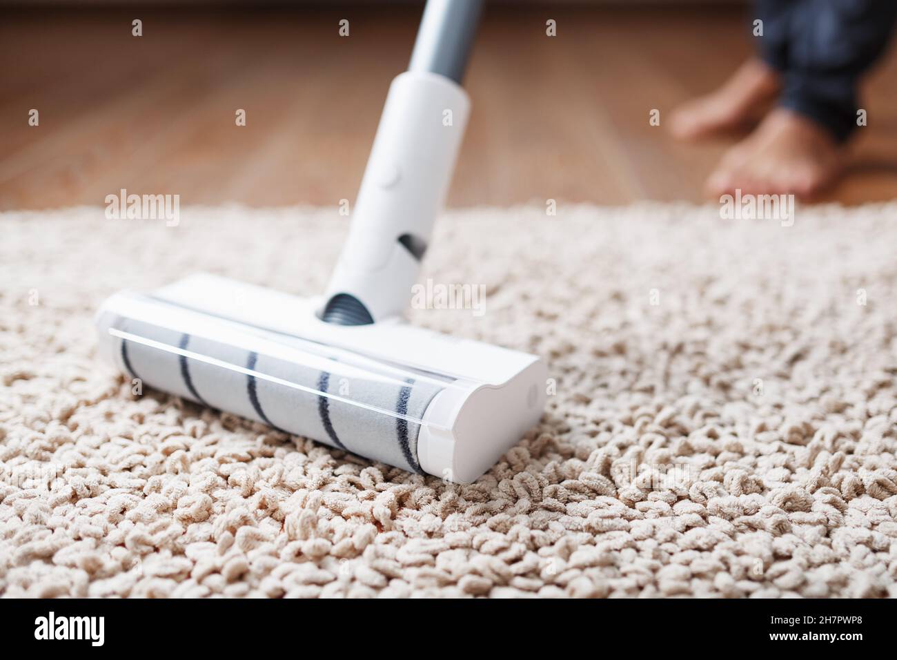 Ein kabelloser Staubsauger reinigt den Teppich im Wohnzimmer mit der Unterseite der Beine. Moderne Technologien für die Reinigung des Hauses. turbo-Bürste Stockfotografie