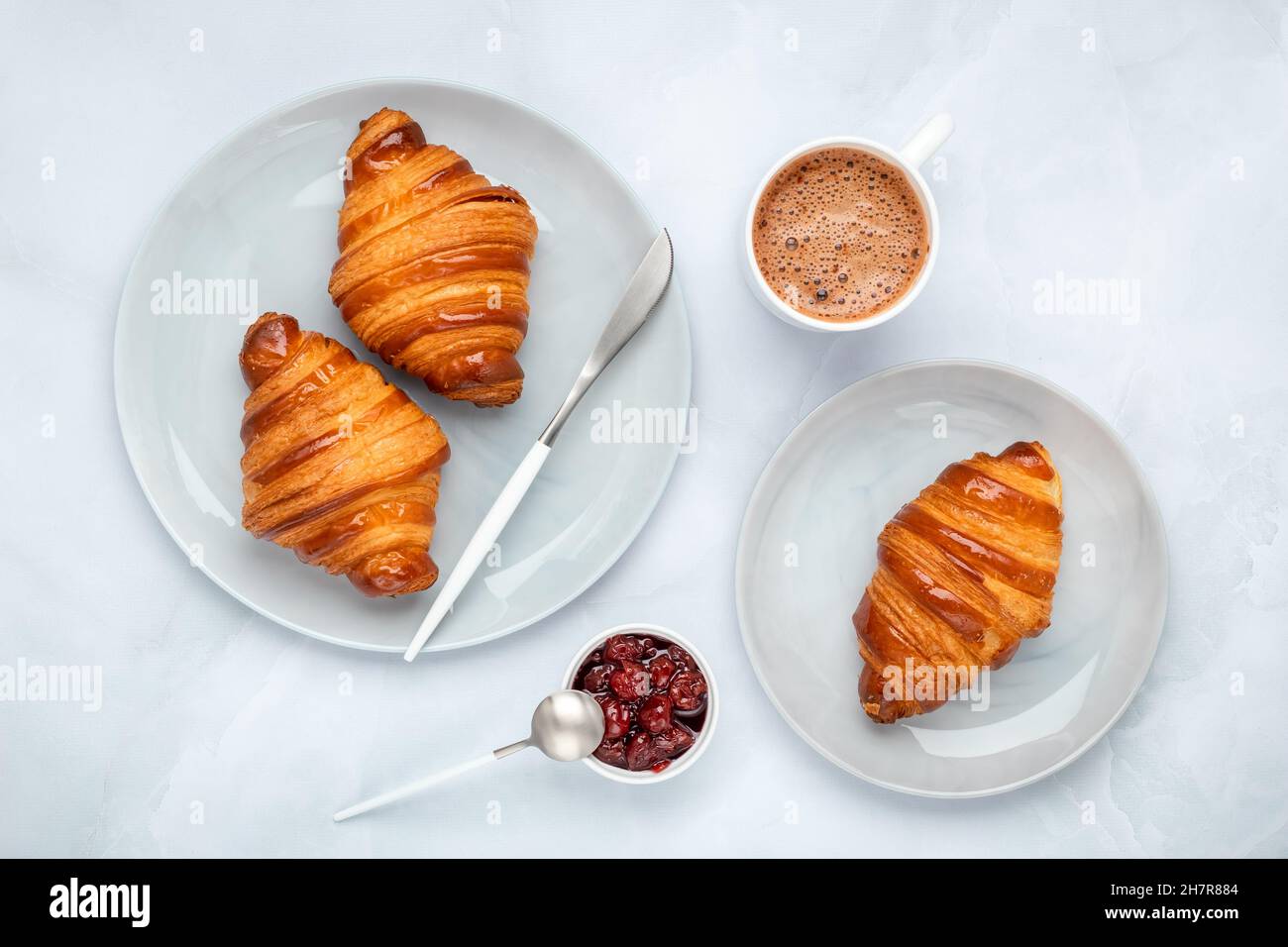 Croissants mit Marmelade und Kaffee. Zwei graue Teller auf einem Marmortisch. Draufsicht, flach liegend. Eine Tasse heiße Schokolade am Morgen zum Frühstück. Französische Cul Stockfoto