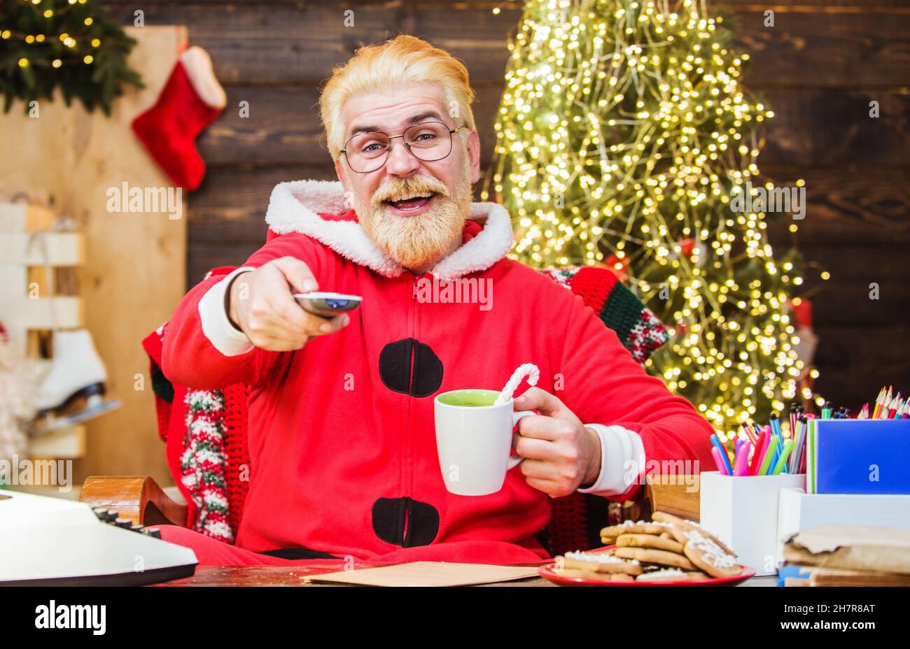 Der Weihnachtsmann sitzt im Sessel und schaut sich einen Weihnachtsfilm an und trinkt Kaffee. Entertainment- und Kinokonzept. Frohes neues Jahr. Stockfoto