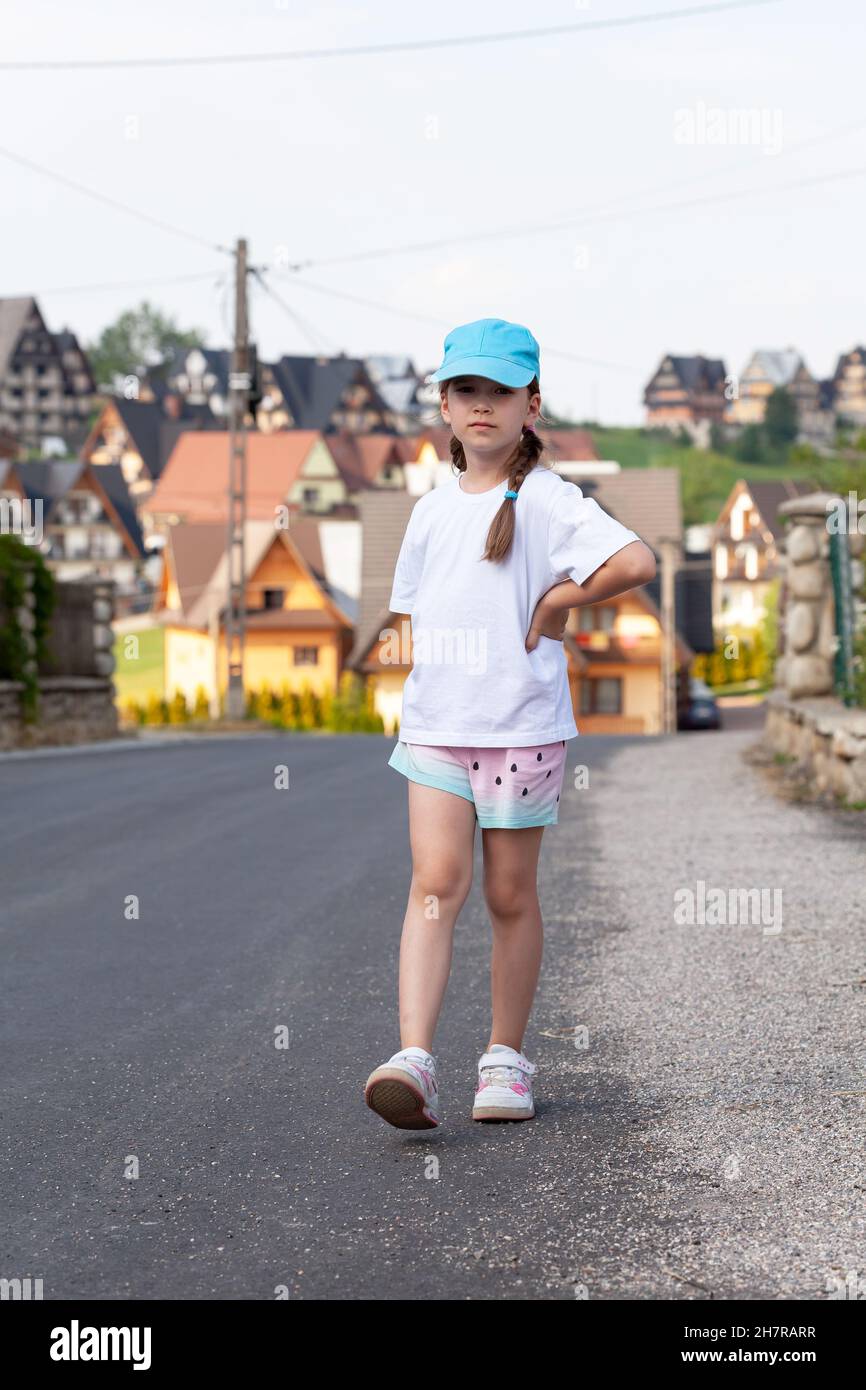 Kind im Grundschulalter, Mädchen im Schulalter, das allein durch eine kleine Stadt geht, spazieren geht, auf der Straße spazieren geht, ländliche Gegend, eine Person, Weißes Hemd, blank, Bas Stockfoto