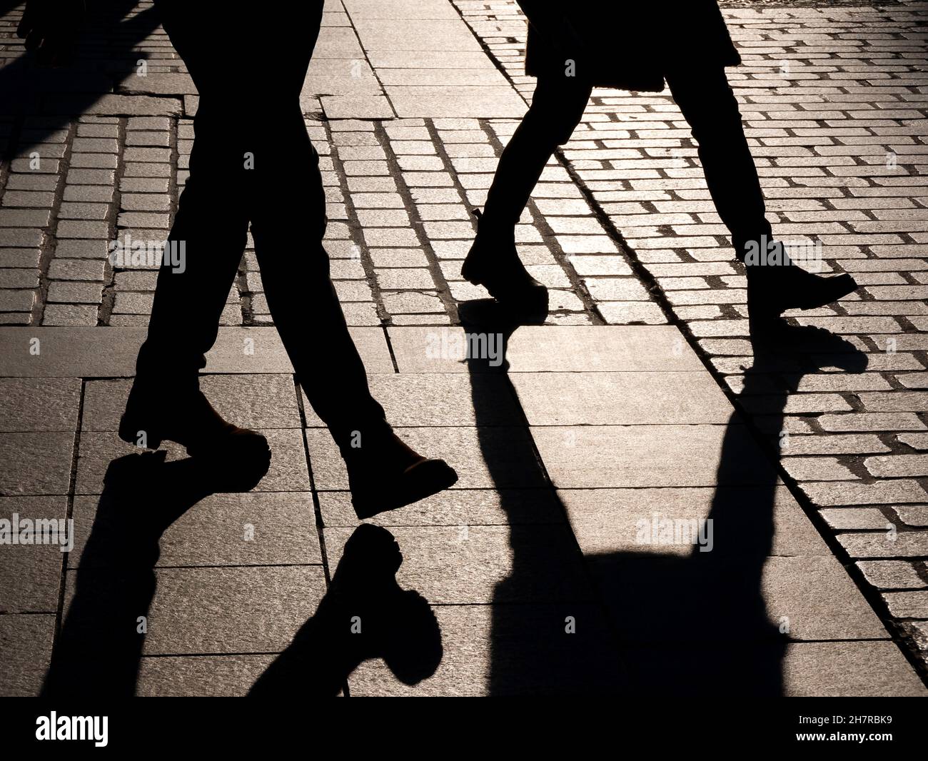 Zwei anonyme, unkenntlich gewordenen Menschen, die durch die Straße gehen, dunkelschwarze Beinumrisse, Schatten. Fußgänger im Freien, Gesellschaft, Anonymität, Lonelin Stockfoto
