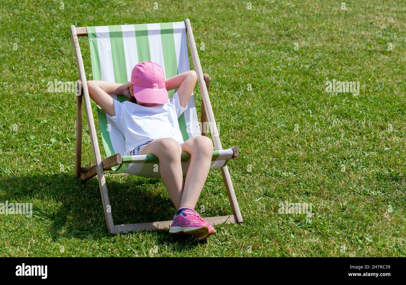 Junge Grundschulkinder, Mädchen, die auf einer Sonnenliege liegen, sich entspannen, schlafen, ein Nickerchen im Garten allein machen. Freizeit, Sommerferien r Stockfoto