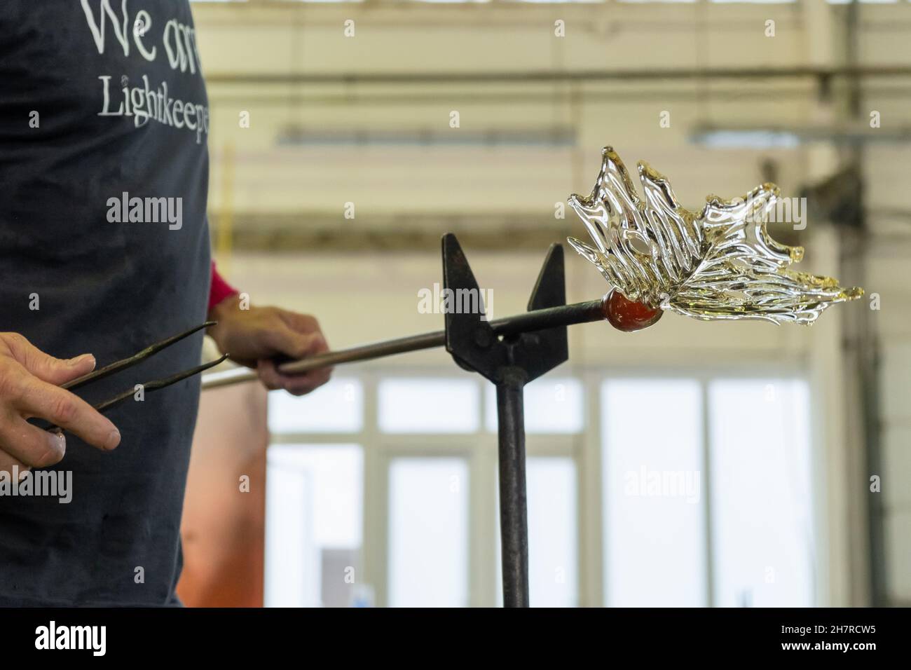 Nahaufnahme Mann macht ein Blatt aus dem Glas für Vase oder Kronleuchter mit Zange und Blasrohr. Stockfoto