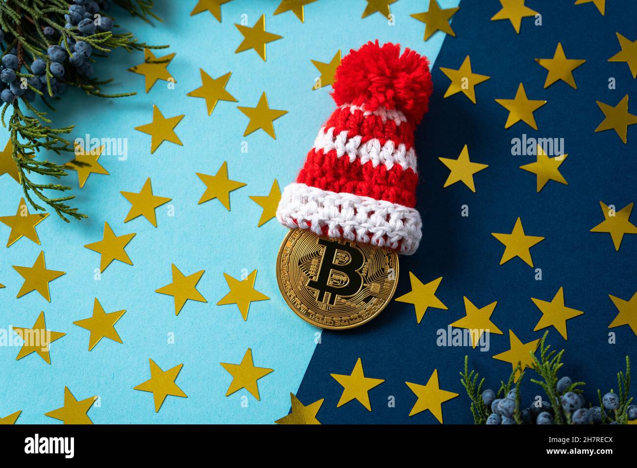 Goldmünze mit Bitcoin-Schild mit Weihnachtskappe auf blauem Hintergrund mit Glitzer und Ästen eines klingenden Baumes. Mining von Kryptowährungen. Stockfoto