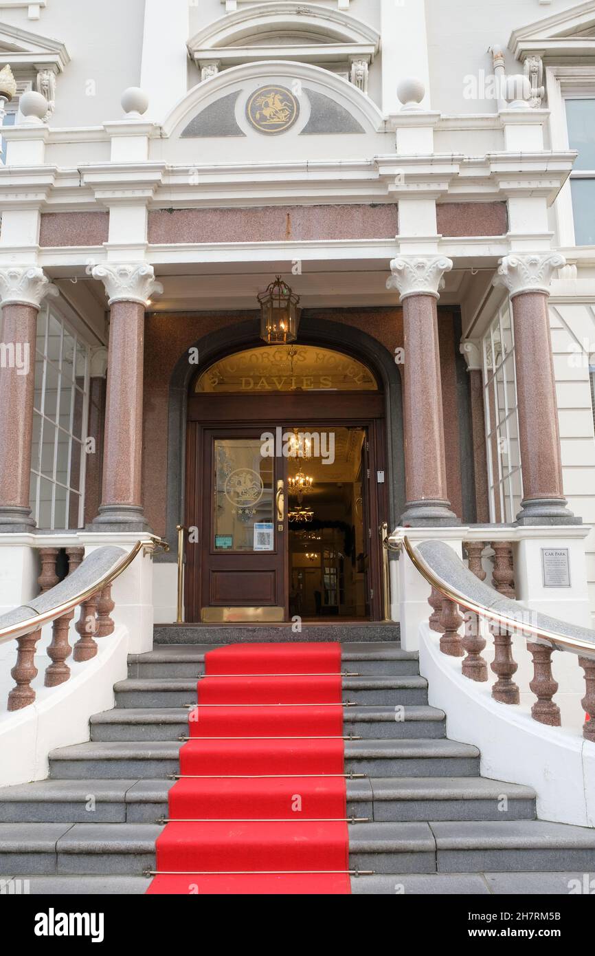 Außenansicht des Eingangs zum St. George's Hotel mit einer geschwungenen, roten Teppichtreppe und Kronleuchtern in der Lobby dahinter. Stockfoto