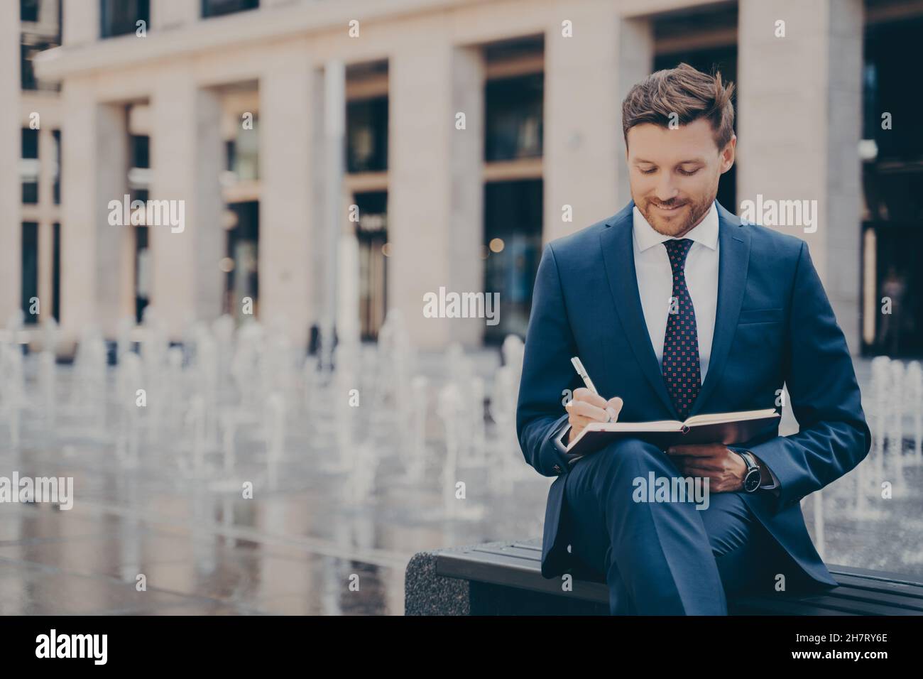 Formell gekleideter Büroangestellter, der seinen Tag in einem Notizbuch organisiert, während er im Freien arbeitet Stockfoto