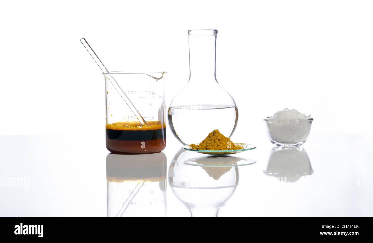 Eisenchlorid-Flüssigkeit mit Rührstab im Becher, kristallklare Flüssigkeit in Flachbodenflasche, organisches Curcuma-Pulver und weiße Flockenchemikalien. Schließenu Stockfoto