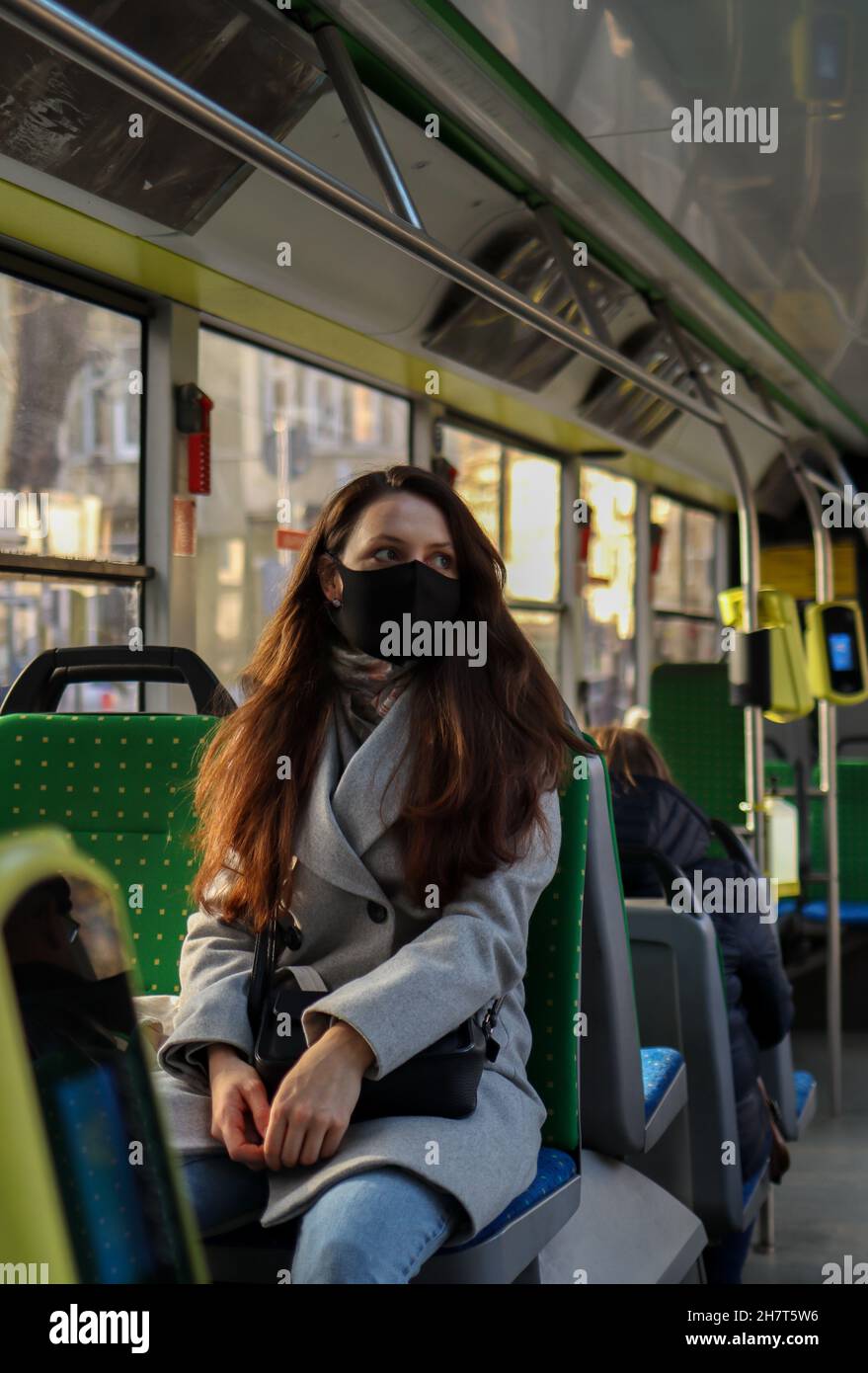 Junge europäische Passagierin mit Gesichtsmaske, wenn sie während der Pandemie von Covid-19 mit dem Bus an überfüllten Orten unterwegs ist. Stockfoto
