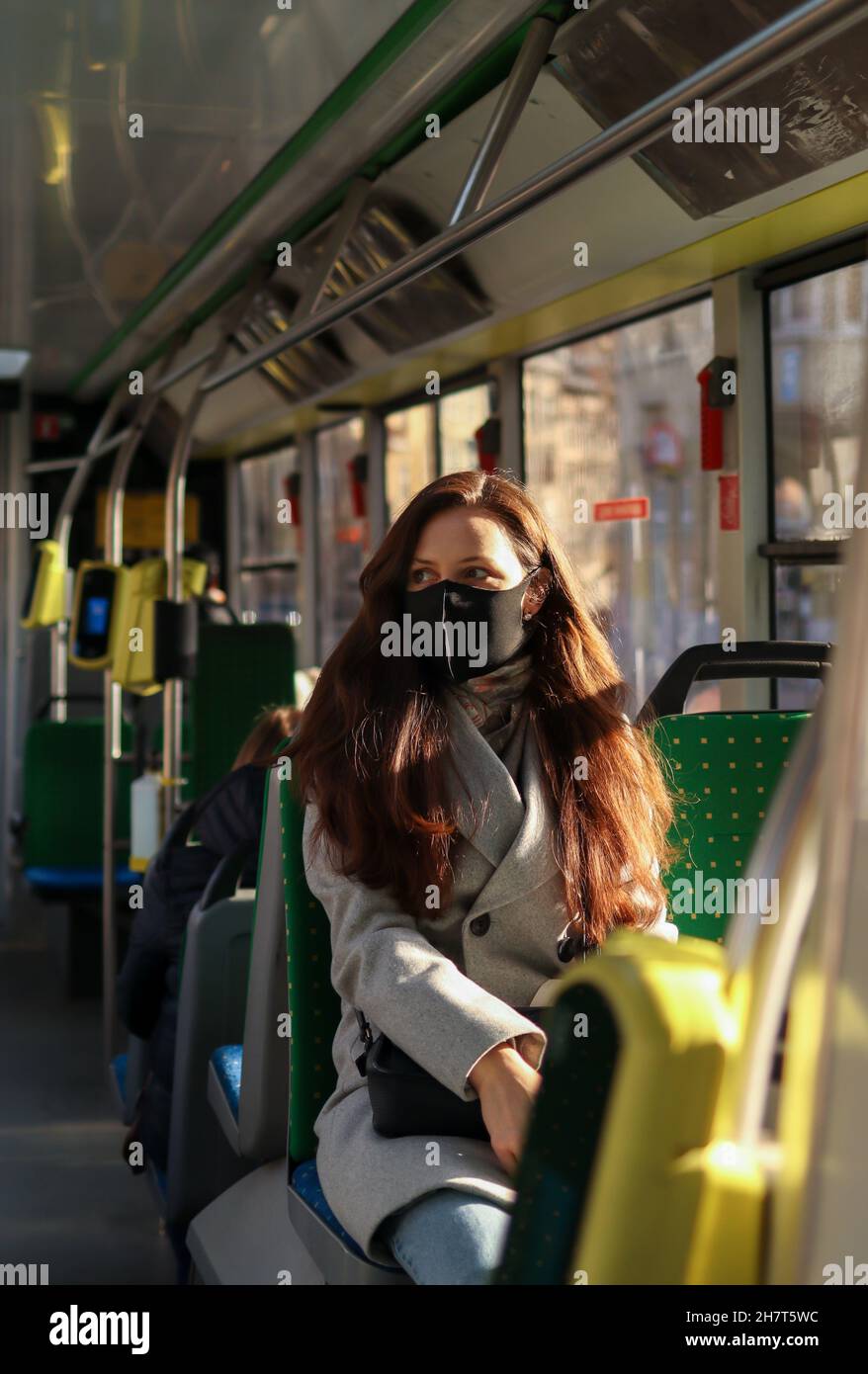 Eine junge Frau mit Atemschutzmaske reist aufgrund einer Coronavirus-Pandemie mit öffentlichen Verkehrsmitteln. Sicherheitsvorkehrungen in Bussen Stockfoto