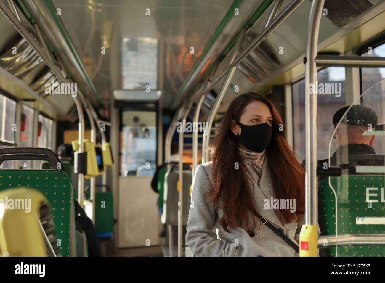 Junge europäische Passagierin mit Gesichtsmaske, wenn sie während der Pandemie von Covid-19 mit dem Bus an überfüllten Orten unterwegs ist. Stockfoto