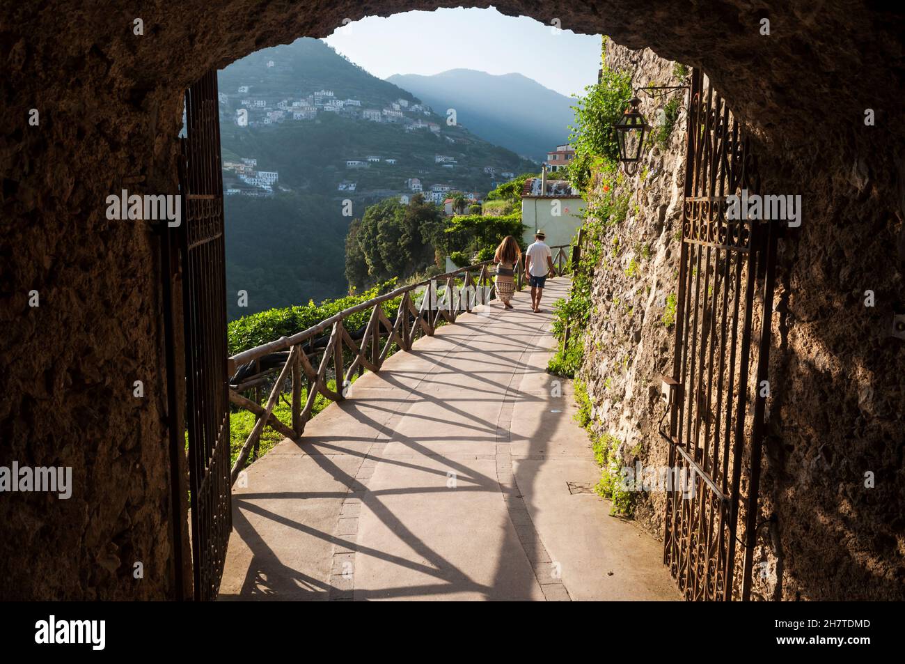 Ein Paar, das an einem schönen Sommernachmittag auf einem Pfad, umrahmt vom Tor der Villa Cimbrone, Ravello, spazieren geht. Auch Blick auf Scala und ferne Hügel. Stockfoto