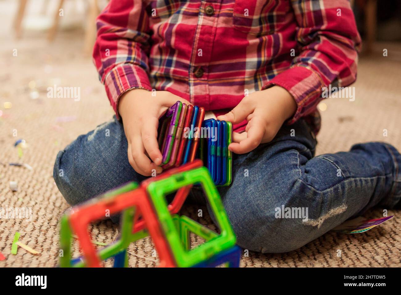 Junge sitzt auf dem Teppich auf dem Boden und spielt mit einem magnetischen Konstruktor Stockfoto