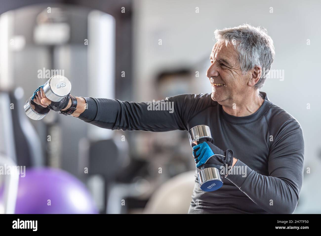 Ein älterer Mann, der mit Hanteln im Fitnessstudio trainieren konnte, lächelte. Stockfoto