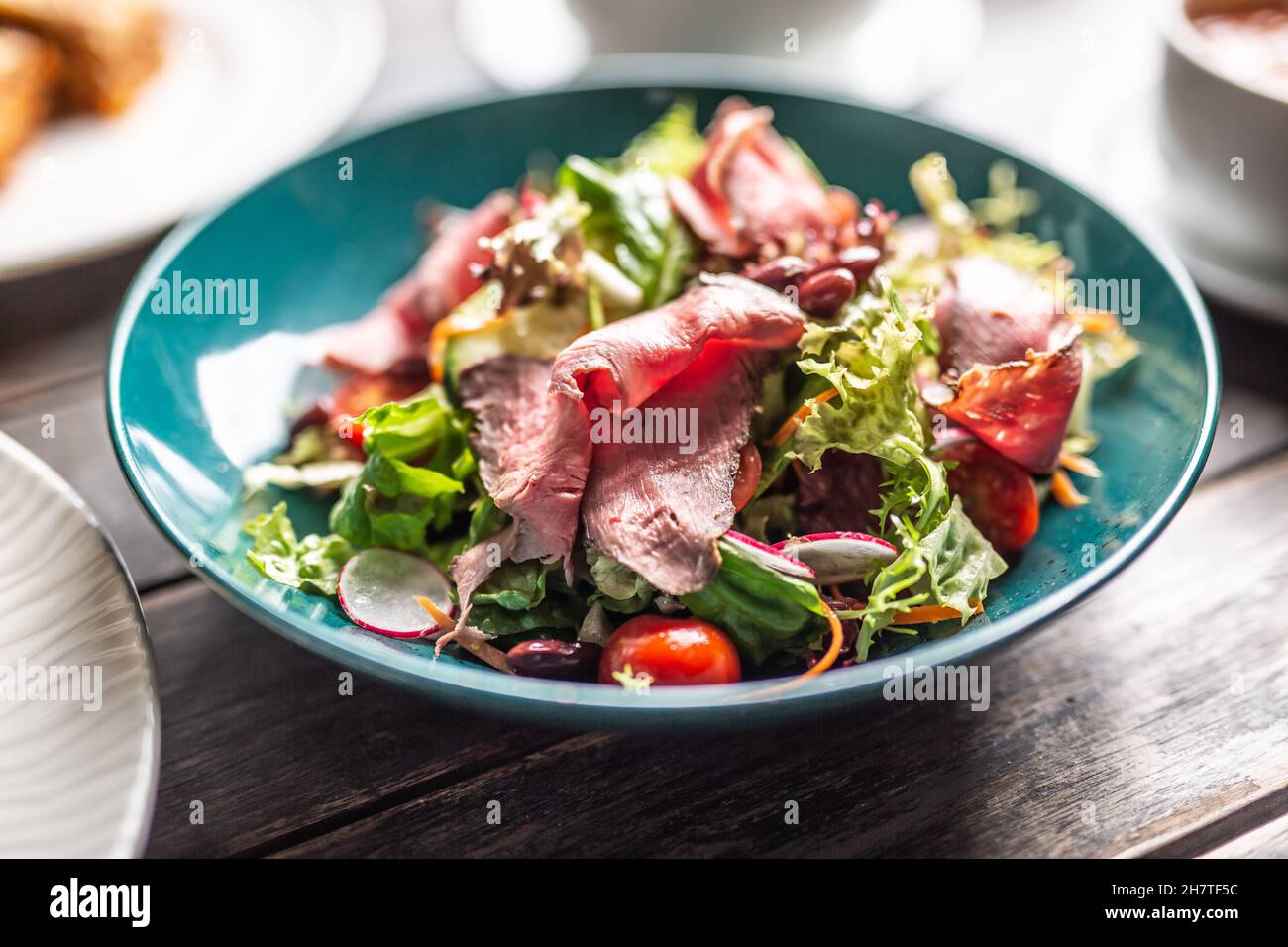 Dünn geschnittenes Roastbeef serviert auf einem knusprigen slad mit Karotten, Kirschtomaten und Radieschen. Stockfoto