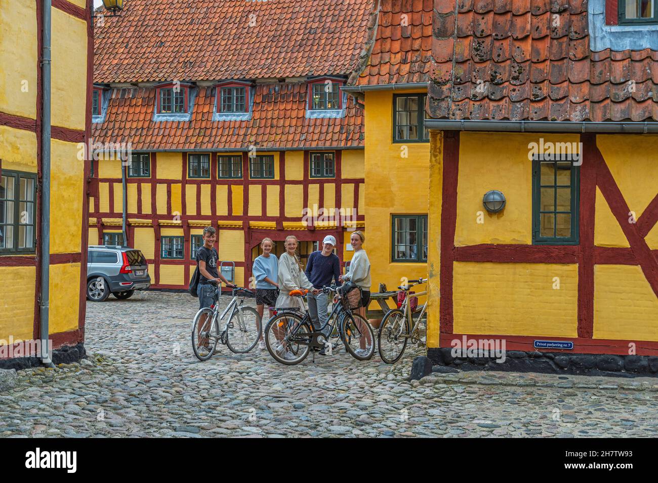 Gruppe von Kindern auf Fahrrädern in der Nähe von traditionellen Fachwerkhäusern und alten gelben Häusern in der Altstadt von Kerteminde. Kerteminde, Dänemark Stockfoto