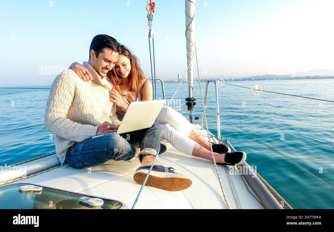 Junges Paar in der Liebe auf dem Segelboot mit Spaß Remote arbeiten am Laptop- glücklicher Luxus-Lifestyle auf Yacht Segelboot - Technologie-Konzept mit Influencer Stockfoto