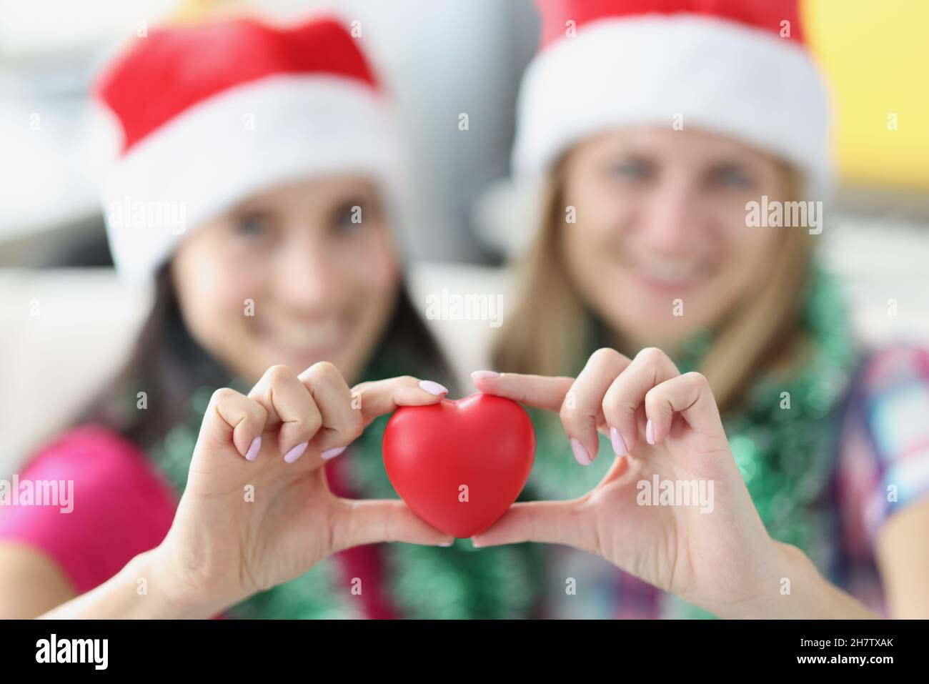 Schwestern halten rotes Herz aus Plastik in den Händen und lächeln Stockfoto