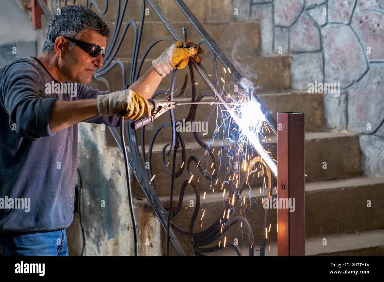 Mann mit Schutzbrille schweißt Metall mit Schweißmaschine. Funken vom Schweißen fliegen zu den Seiten. Stockfoto