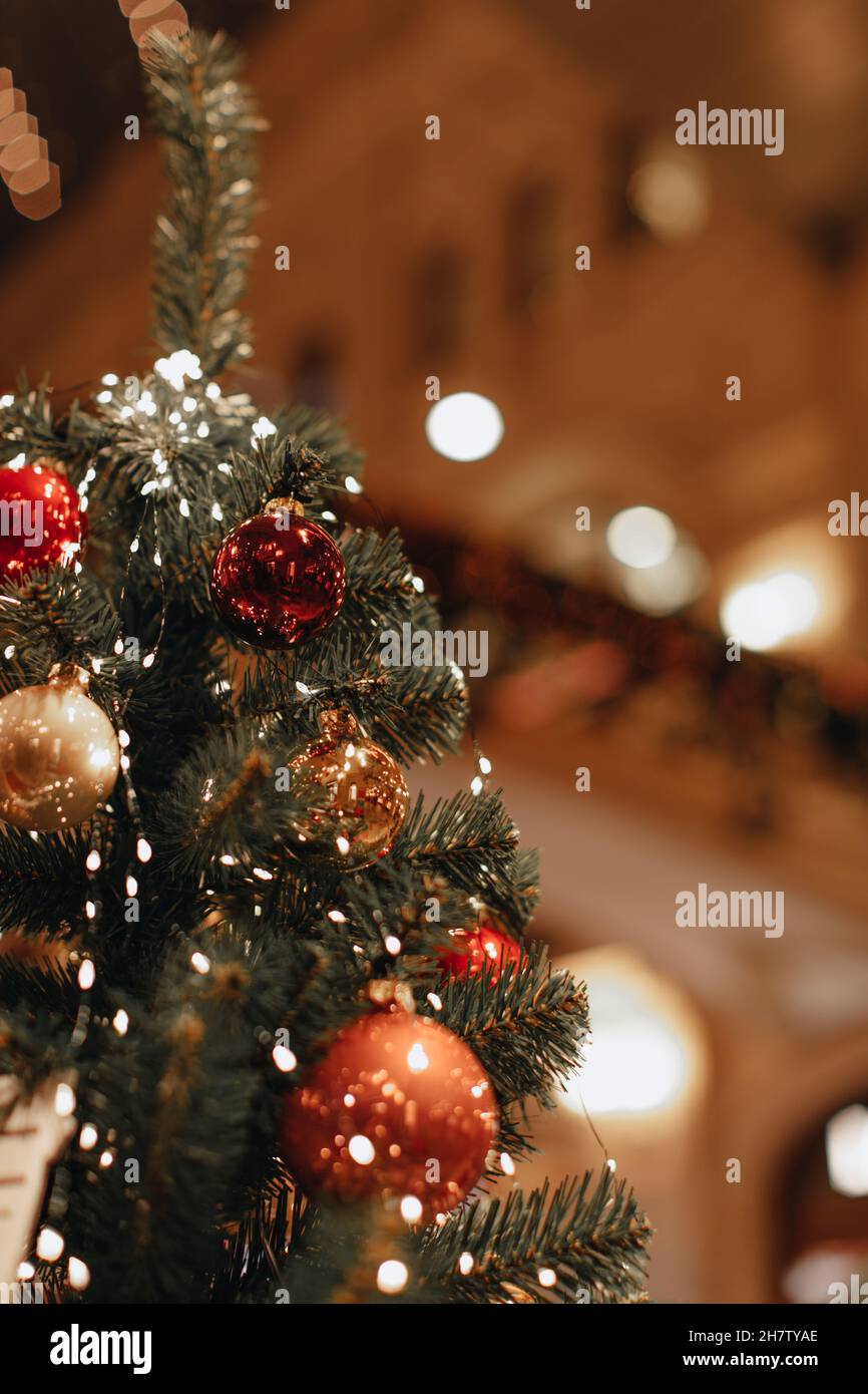 Rot glänzende Weihnachtskugeln hängen auf dem Weihnachtsbaum. Neujahrsdetails in festlicher Atmosphäre mit magischen Bokeh-Lichtern Stockfoto