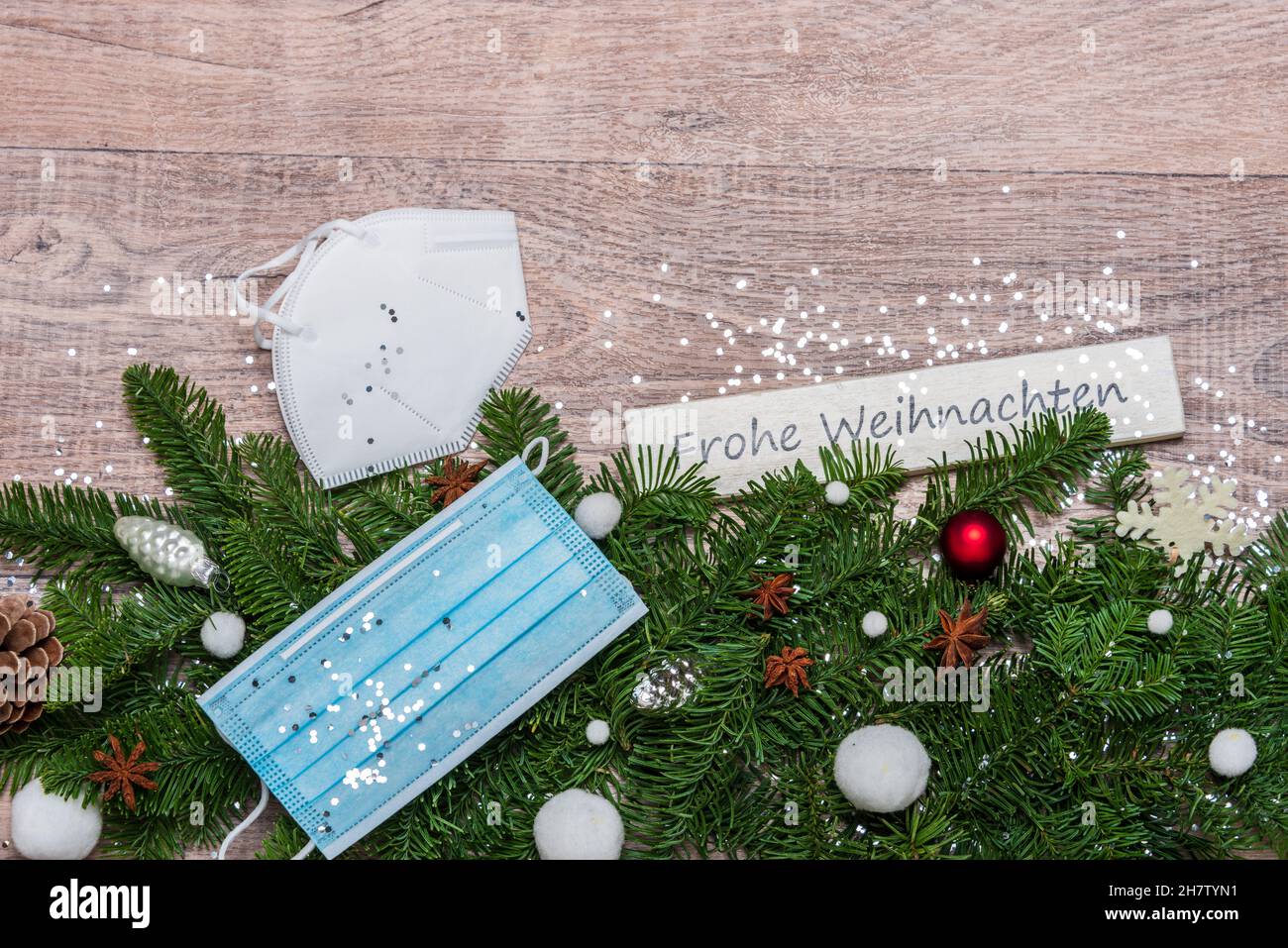 Weihnachtsdekoration mit grünen Tannenzweigen, Corona Alltagsmasken und einem Schild 'Frohe Weihnachten' Stockfoto