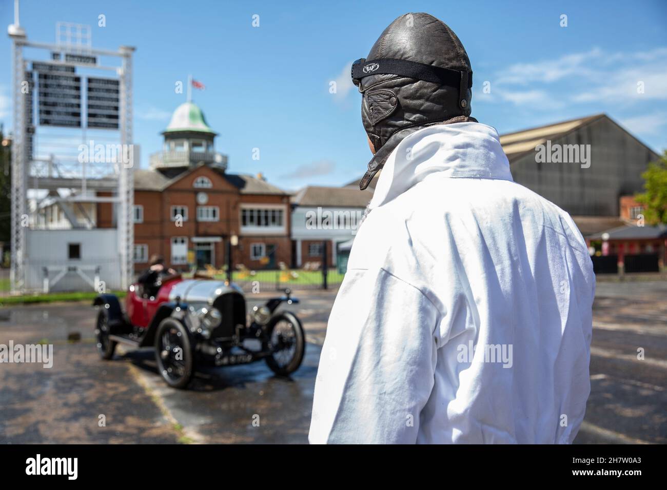 Ein Fahrer, der eine klassische Brille und Overalls trägt und einen klassischen Bentley-Wagen in Brooklands, der ersten eigens für diesen Zweck gebauten Rennstrecke der Welt, England, anschaut. Stockfoto