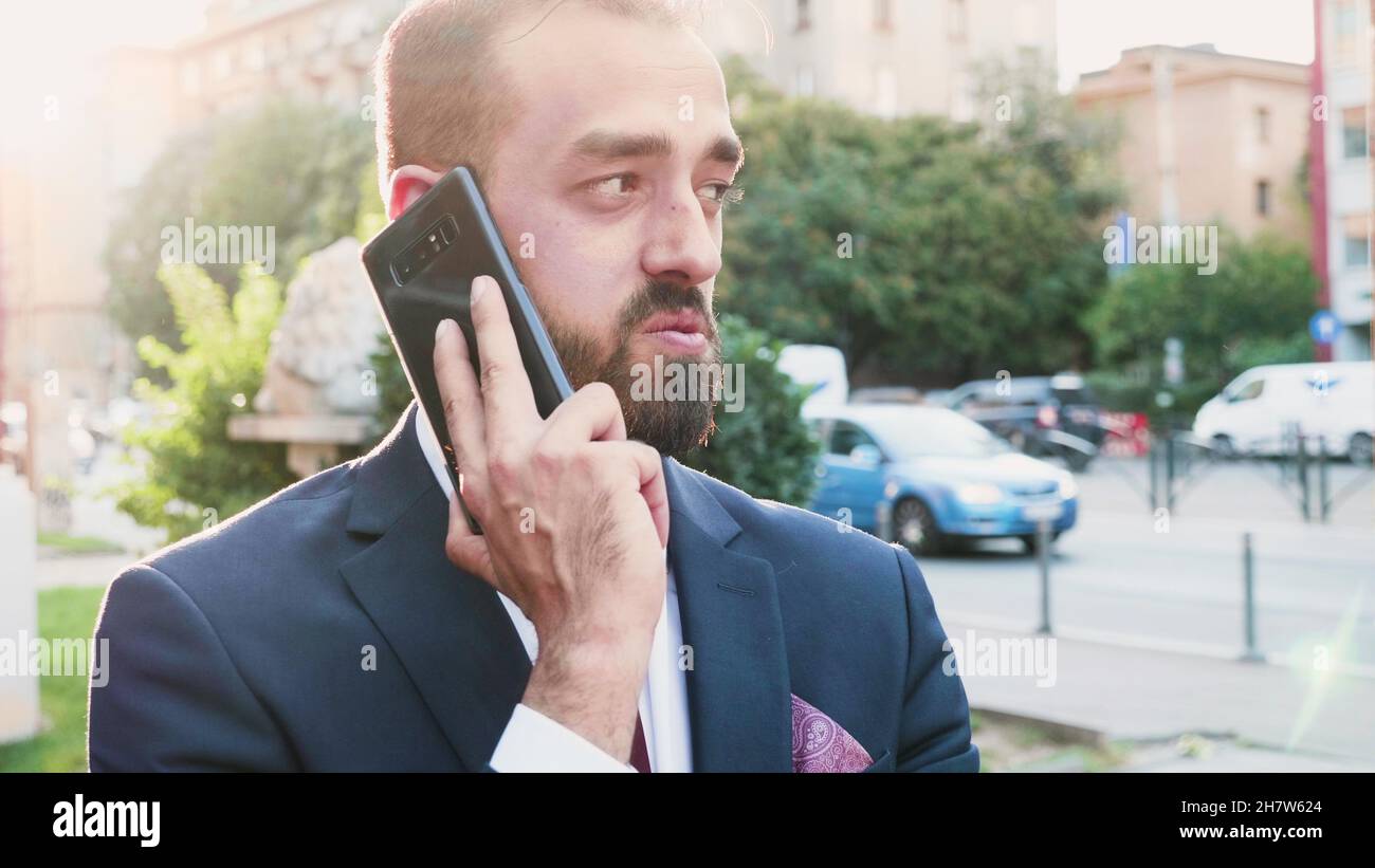 Porträt eines Geschäftsmannes, der am Telefon über die Managementstrategie mit einem Remote-Unternehmer spricht. Der Manager löst Meinungsverschiedenheiten vor dem Bürogebäude. Outdoor-Konzept Stockfoto