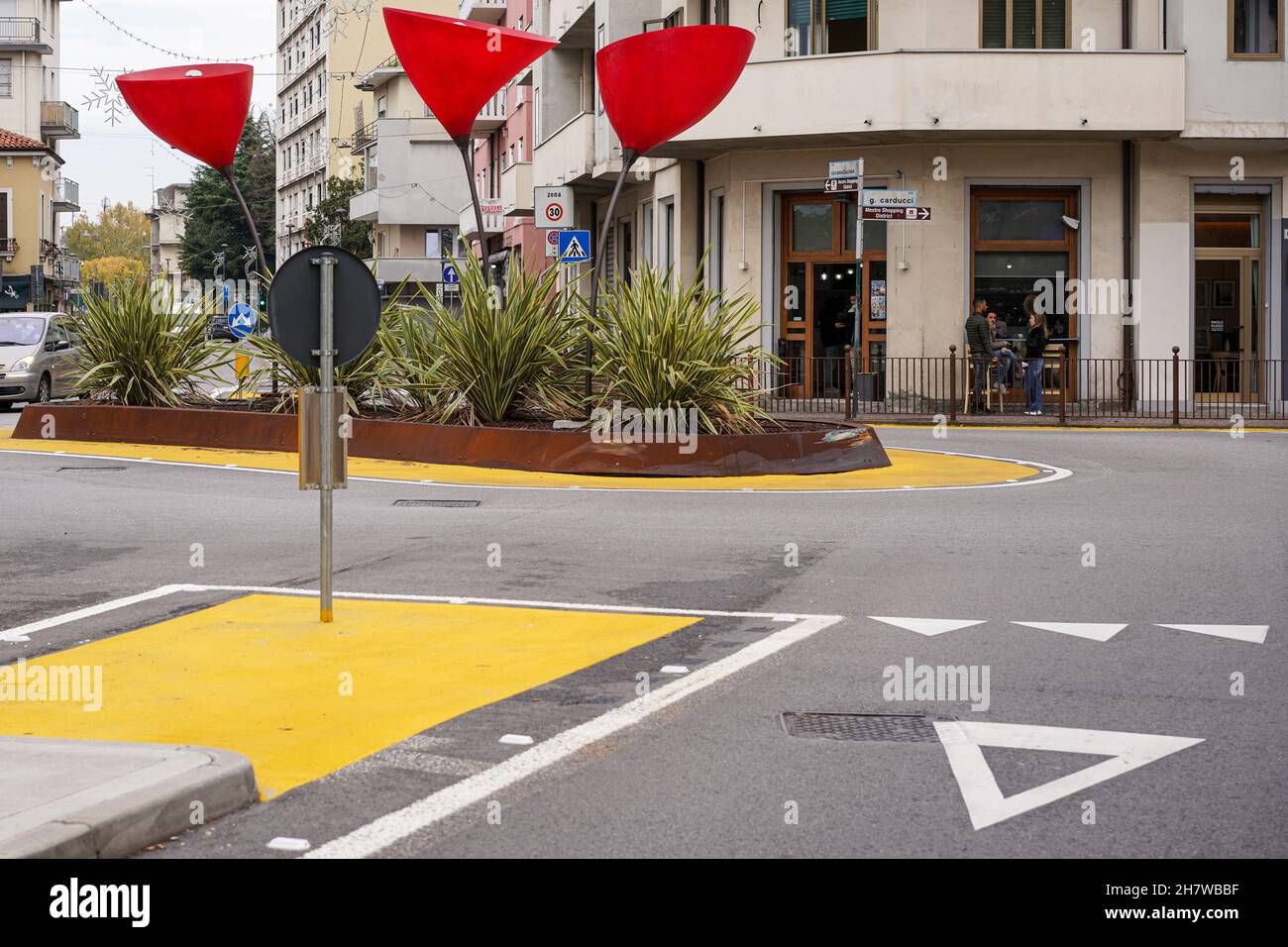 Straßenszene in Venedig Mestre. Gebogene Lampen mit großen roten Farbtönen stehen auf einer Verkehrsinsel. Rund um die Insel ist eine gelbe Abgrenzung. Stockfoto