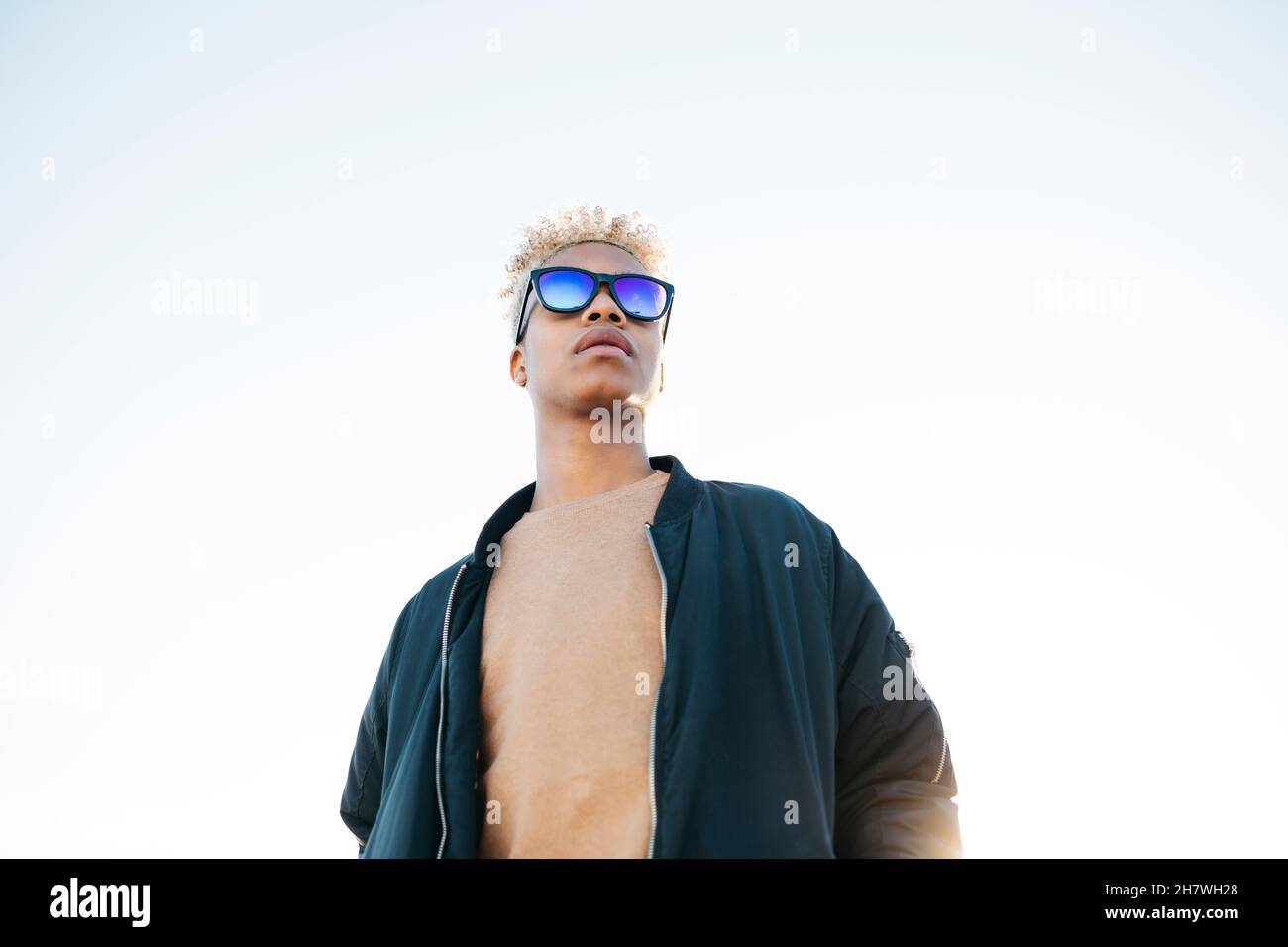 Junger lateinamerikanischer Mann mit blauer Sonnenbrille am weißen Himmel Stockfoto