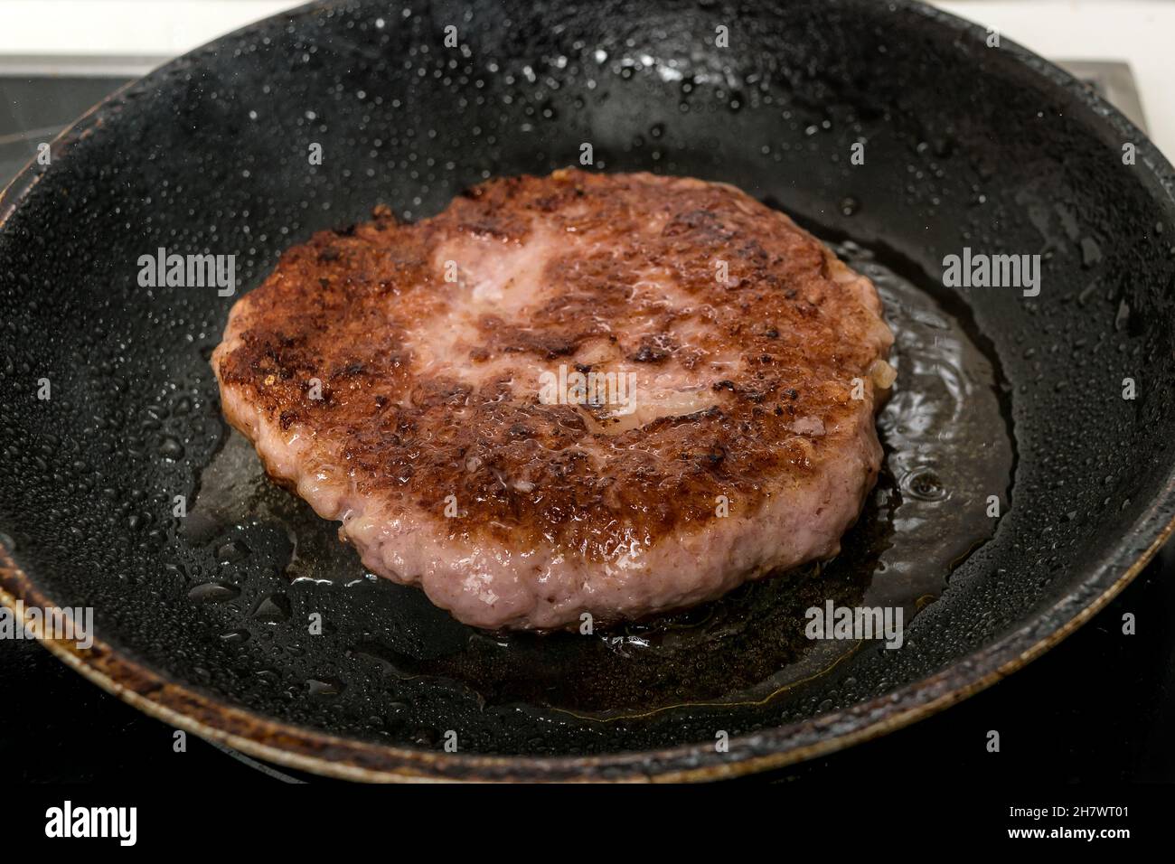 Rohe Burger Patty in einer eisernen Pfanne bereit zu braten, einige Burger-Zutaten  im Hintergrund Stockfotografie - Alamy